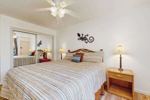 A bedroom with a bed, bedside lamps, a ceiling fan, a mirror, and a wall decal. - NEW Fall Deal Sea-View Kihei Condo for Four Across from Kamaole III (Kihei)