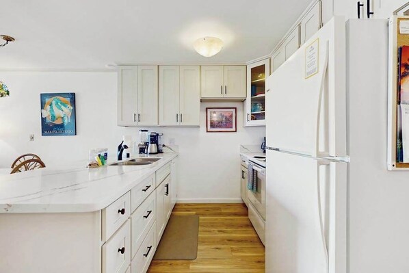 A compact kitchen with white cabinets, a marble countertop, and a wooden floor. - NEW Fall Deal Sea-View Kihei Condo for Four Across from Kamaole III (Kihei)