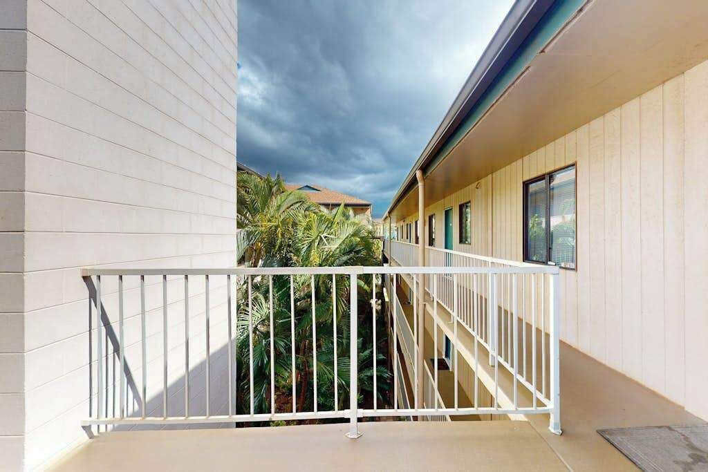 Un balcon avec une balustrade blanche, une vue sur des palmiers et un bâtiment aux murs recouverts d’un revêtement de couleur beige.