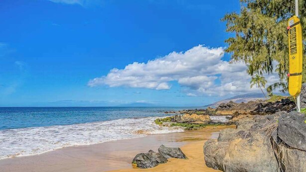 Una playa con cielos despejados, un puesto de salvavidas amarillo y grandes rocas.