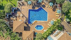 Vista aérea de un resort con piscina central, varias zonas de descanso y un jacuzzi pequeño.