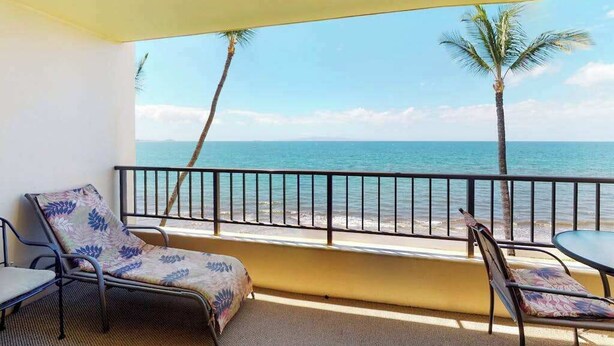 Un balcon avec deux fauteuils, une petite table et une vue sur l’océan, bordé de palmiers.