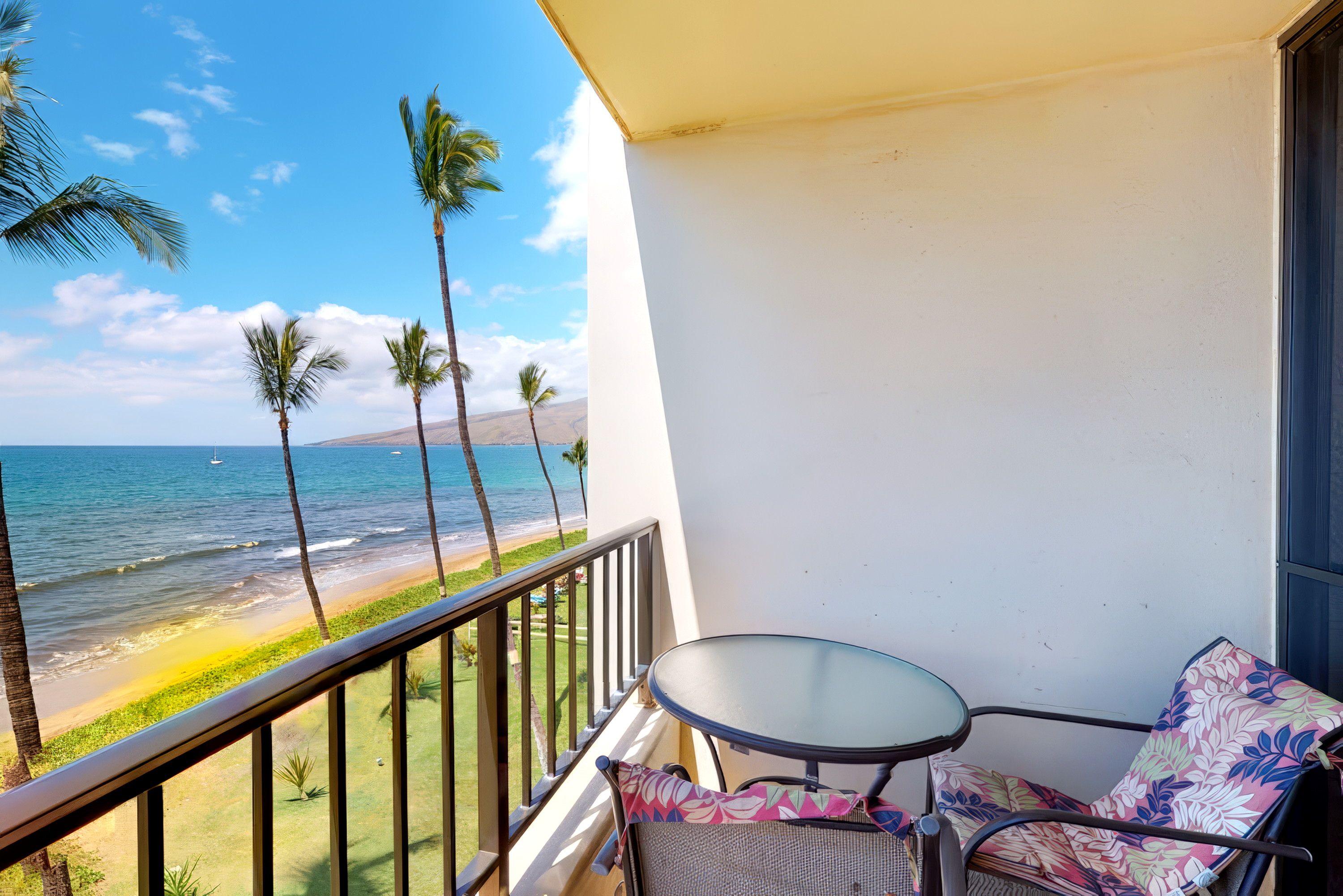 A balcony with a view of the beach and ocean, a small table, and a chair.