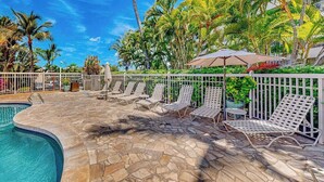 Un espace piscine doté de chaises longues, d’une terrasse en pierre et de palmiers.