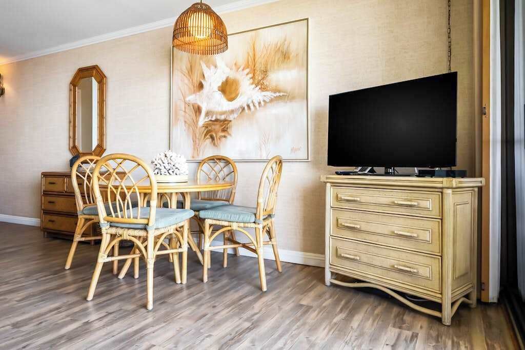Un coin repas avec une table et des chaises en bois, un téléviseur posé sur un meuble, et une grande œuvre d’art encadrée accrochée au mur.