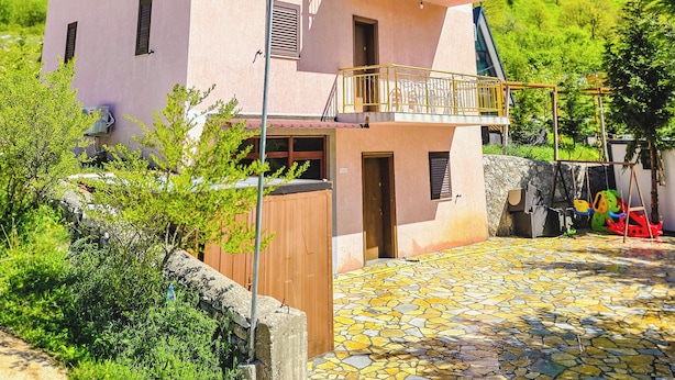 Un bâtiment à deux étages doté d’un balcon, d’un mur en pierre et ayant une chaîne de montagnes en arrière-plan.