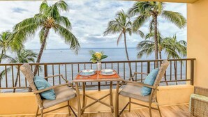 Un balcon avec une table dressée pour deux personnes, donnant sur une plage bordée de palmiers et sur l’océan.