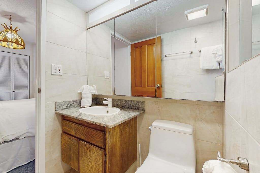 Een badkamer met een houten wastafelmeubel, een wastafel, toilet, spiegel en een handdoekhouder.