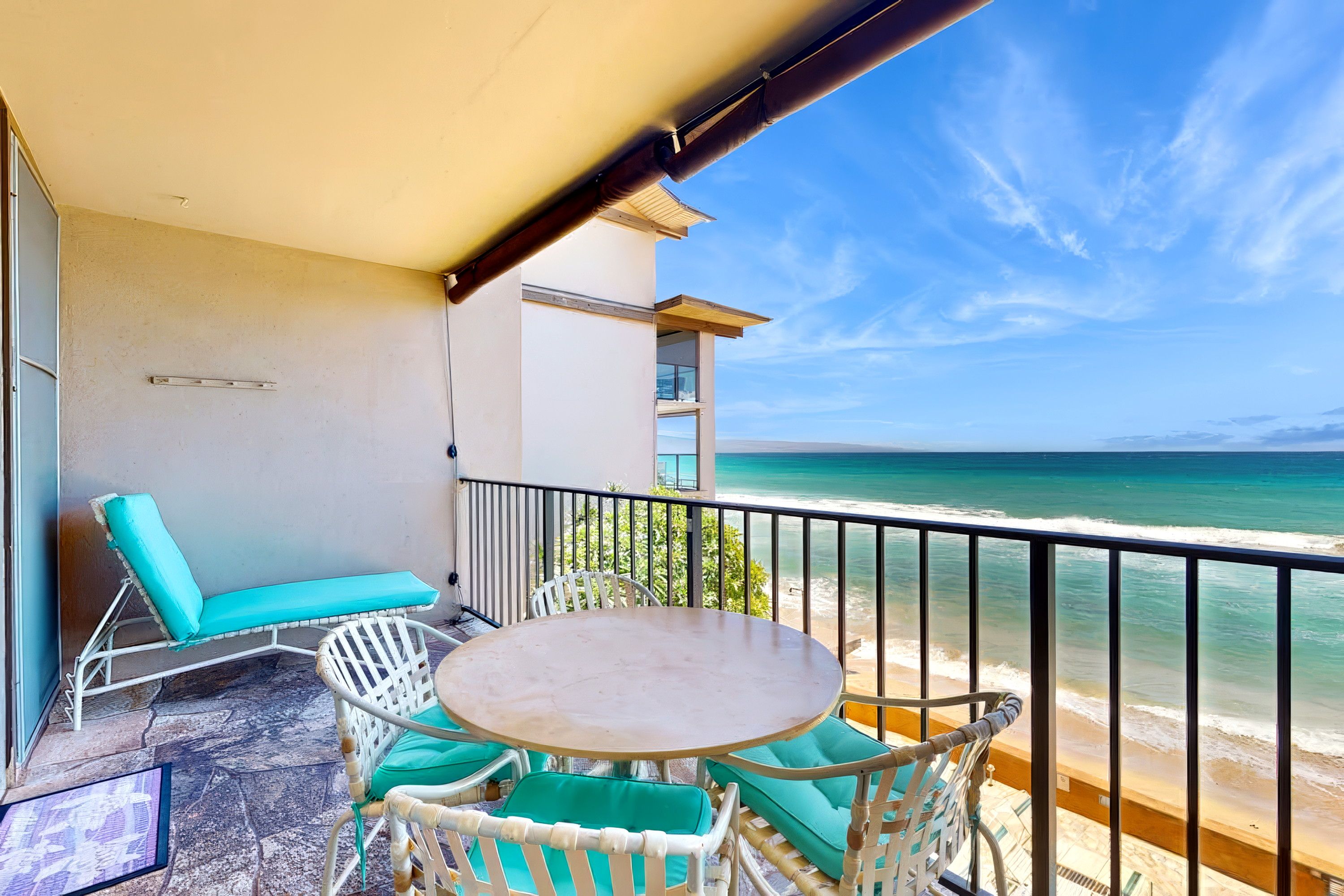 A balcony with a table and chairs, overlooking a beach and ocean.