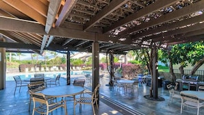 Un patio al aire libre con mesas y sillas, una parrilla y una piscina al fondo.