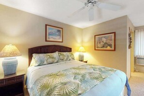 A bedroom with a bed, two bedside lamps, a ceiling fan, and two framed pictures on the wall. - Relaxing 2BR Kihei Condo Near Beach with Pool and Hot Tub (Kihei)