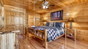 Une chambre dans une cabane en bois, avec un lit, un ventilateur de plafond et un tableau accroché au mur.