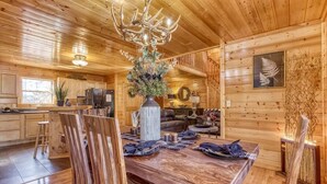 Un intérieur en bois comprenant une table à manger, des chaises, un lustre et un coin cuisine.