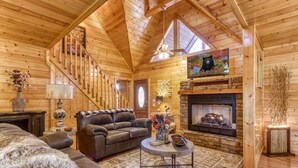 L’intérieur d’une cabane en rondins, avec une cheminée, un canapé en cuir et un escalier.