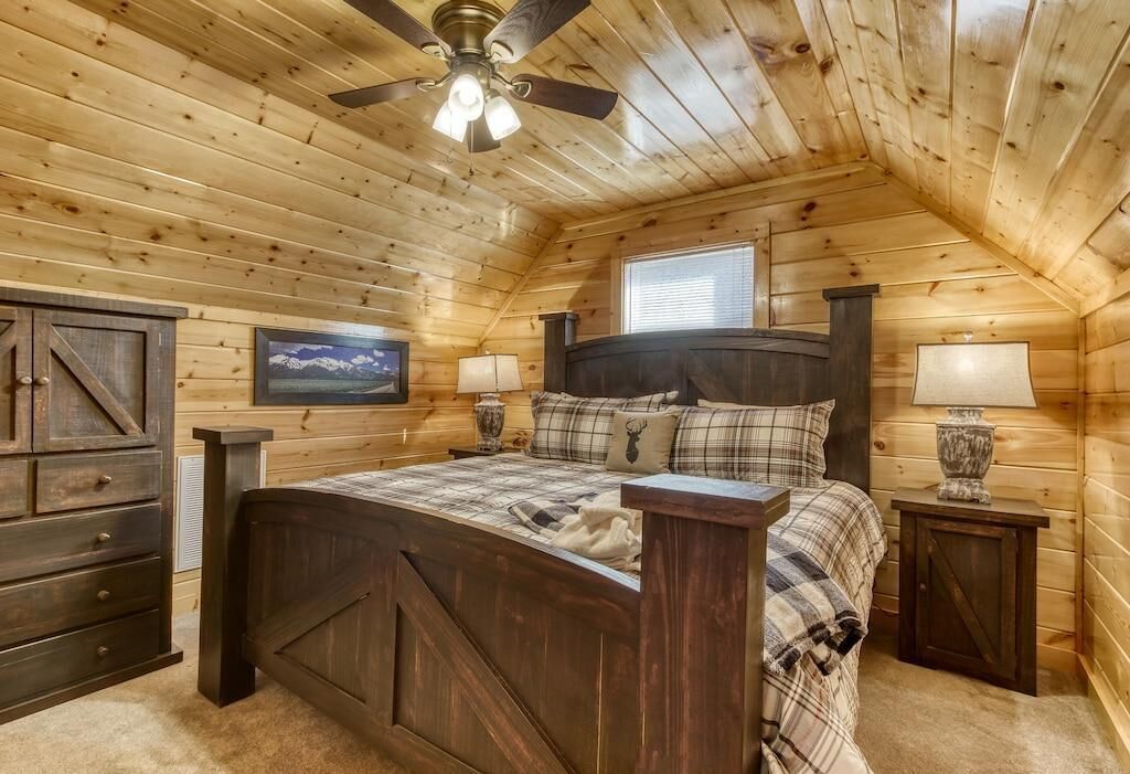 Camera da letto in una baita di legno, con un letto, due comodini, una ventola a soffitto e una finestra.