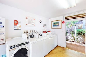 A laundry area with multiple washing machines, a clock, and a framed painting on the wall. - Beachside Fun at Mahina Surf Resort Condo - Pool, Laundry, Near Local Activities (Lahaina)