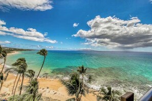 Uma praia com águas turquesa cristalinas, palmeiras e uma linha de costa distante.