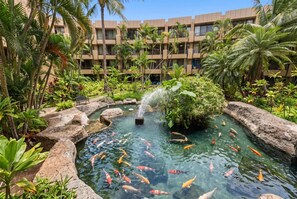 A hotel courtyard with a koi pond, palm trees, and a water feature. - NEW Oceanfront West Maui Retreat with Pool and Hot Tub (Lahaina)