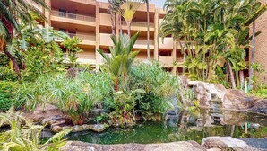 Ein Hotel mit Pool, umgeben von üppiger tropischer Vegetation und einem mehrstöckigen Gebäude im Hintergrund.