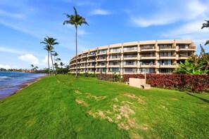 Ein Strandhotel mit mehreren Balkonen, einem gepflegten Rasen und Palmen.
