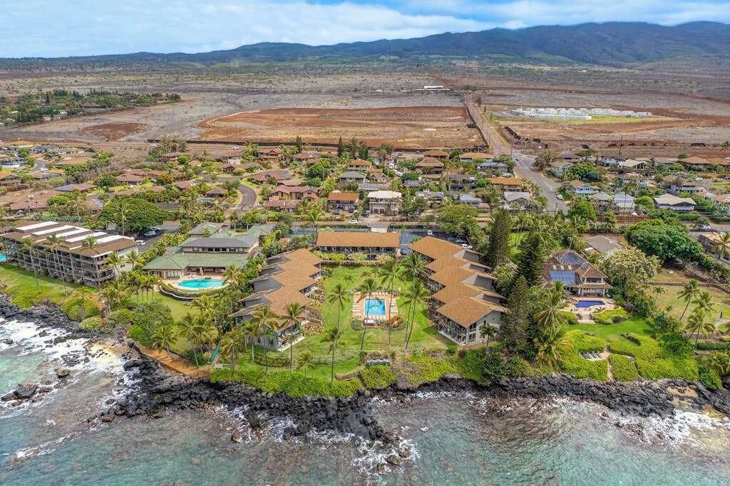 Vista aérea de un resort con varias construcciones, una piscina y una costa.