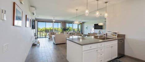 Een moderne keuken met een groot eiland, hangende lampen en uitzicht op de omgeving.