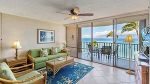 Ein Zimmer mit einem grünen Sofa, einem Couchtisch, einem Deckenventilator und Meerblick durch eine Schiebetür.