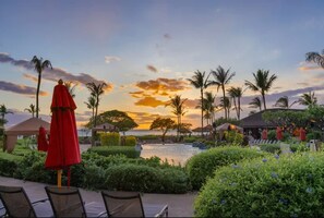 Een resort met een zwembad, palmbomen en uitzicht op de zonsondergang.