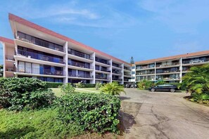 Ein mehrstöckiges Hotel mit Balkonen, einem Parkplatz und üppiger Bepflanzung.