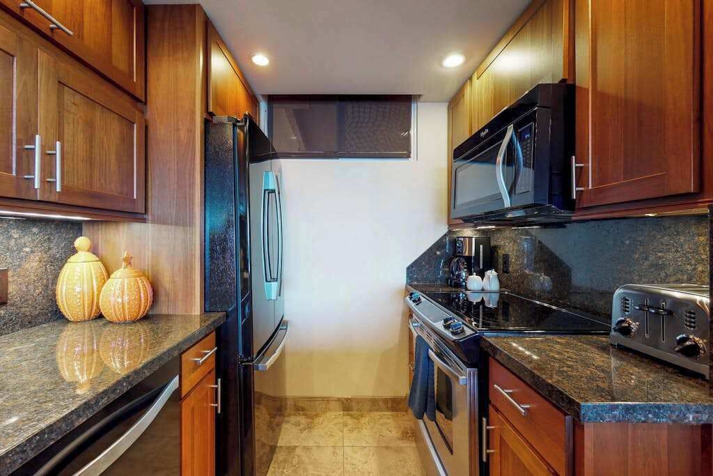 A kitchen with wooden cabinets, a black refrigerator, a microwave, a stove, and granite countertops.