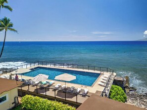 Un espace piscine avec vue sur l’océan, des chaises longues et des parasols.