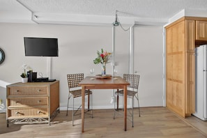 A dining area with a wooden table, wicker furniture, and a flat-screen TV mounted on the wall. - *New* Fall Sale Connecting Honokowai Ocean-View Suites for Eight (Lahaina)