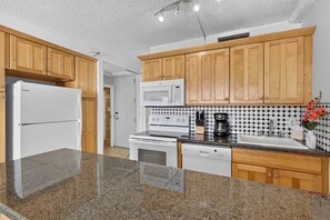 A kitchen with wooden cabinets, a white refrigerator, a microwave, a stove, and a sink. - *New* Fall Sale Connecting Honokowai Ocean-View Suites for Eight (Lahaina)