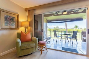 A room with a green sofa, a small stool, a table with chairs, and a sliding glass door leading to an outdoor patio with a table and chairs. - NEW Kaanapali Studio with Golf and Ocean Views Near the Beach (Lahaina)