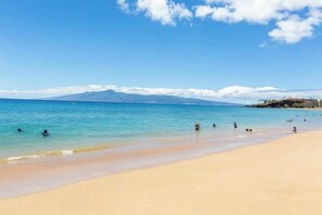 A beach with clear water, people swimming, and a mountain in the background. - NEW Kaanapali Studio with Golf and Ocean Views Near the Beach (Lahaina)