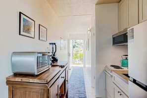 A narrow kitchen with a microwave, toaster, and stove. There are framed pictures on the wall and a door leading to a balcony. - Kihei Studio Retreat at Keawakapu Beach- Kitchen, Laundry, Ocean/Mountain Views (Kihei)