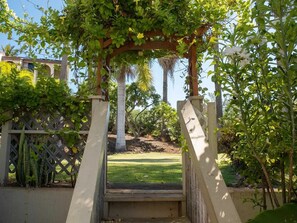 A garden with a pergola structure, a pathway leading to a grassy area, and a fence with climbing plants. - Kihei Studio Retreat at Keawakapu Beach- Kitchen, Laundry, Ocean/Mountain Views (Kihei)