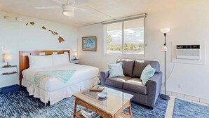 Une chambre d’hôtel équipée d’un lit, d’un canapé, d’une table basse, d’un ventilateur de plafond, d’une fenêtre avec vue et d’un climatiseur fixé au mur.
