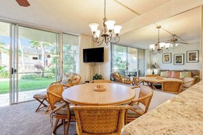 A spacious living area with a large sliding glass door leading to a patio, a round wooden table with wicker chairs, a sofa with cushions, and a ceiling fan. - *New* Fall Special Garden Lanai Retreat Near Kamaole II (Kihei)