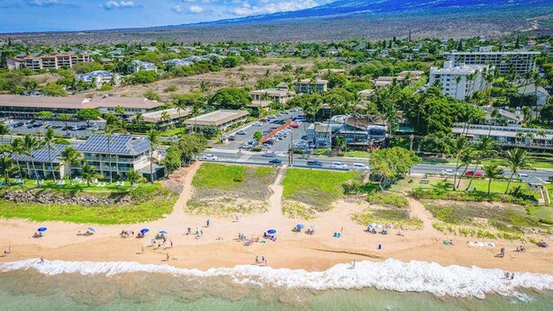 An aerial view of a coastal resort area with buildings, a beach, and a mountain in the background. - *New* Fall Special Garden Lanai Retreat Near Kamaole II (Kihei)