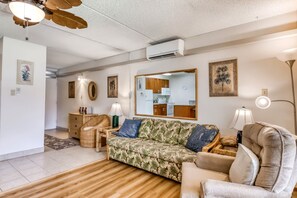 Ein Wohnzimmer mit einer Couch, einem Couchtisch und einem Essbereich, wobei sich im Hintergrund eine Küche befindet.