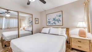 Una habitación de hotel con una cama grande, una mesita de noche con lámpara, un ventilador de techo y un espejo amplio.