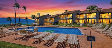 A resort with a pool, lounge chairs, and a sunset view.