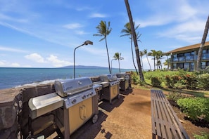 Ein Strand mit einer Grillstation, Palmen und einem Gebäude im Hintergrund.