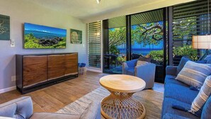 Una sala de estar moderna con un mueble de madera, una mesa redonda de mimbre, un sofá azul y un ventanal con vista al océano.