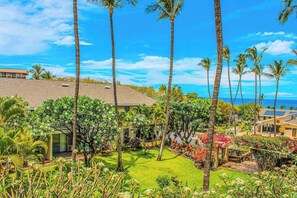 A tropical garden with palm trees and a view of the ocean. - *NEW* Fall Deal Top-Floor Ocean View by Kamaole II (Kihei)