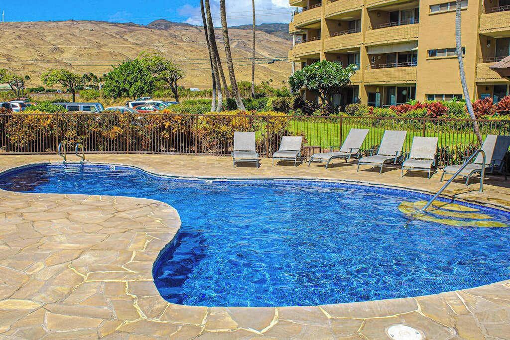 A swimming pool with lounge chairs, a stone deck, and a building with balconies in the background.