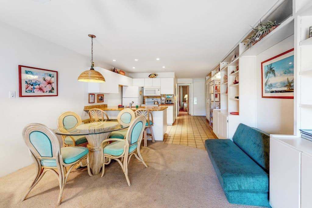 Une cuisine moderne avec des meubles blancs, un coin repas avec des chaises en osier et un canapé de couleur turquoise.