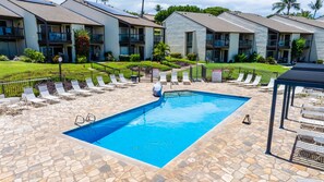 Una piscina con sillas de descanso y una zona de estar cubierta, rodeada por una terraza de baldosas de piedra y una valla baja.