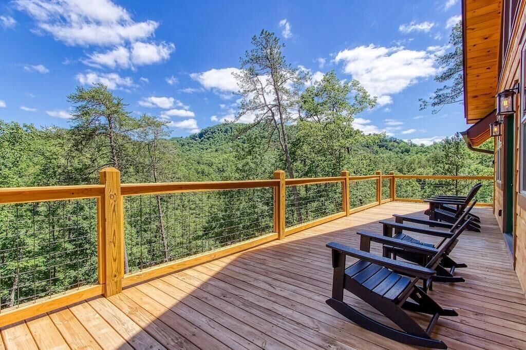 Um deck de madeira com guarda-corpo, área de estar ao ar livre e vista para uma área arborizada.